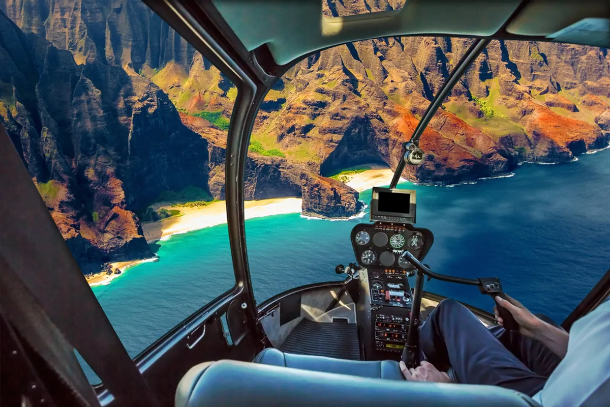 Helicopter flying over Kauai's Na Pali Coast with dramatic emerald cliffs, cascading waterfalls, and turquoise ocean