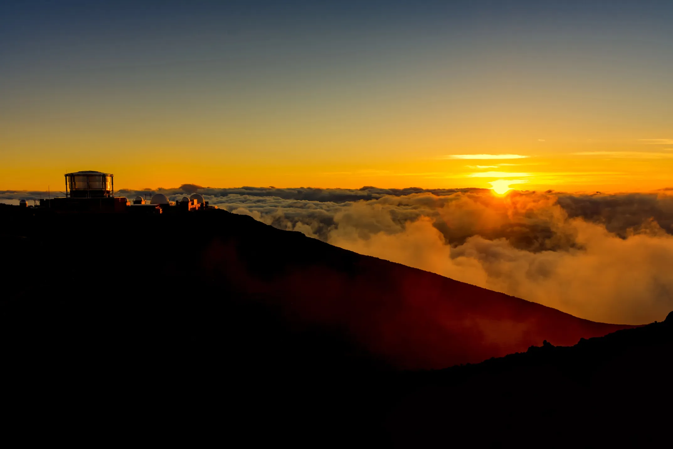 Spectacular sunrise view from Haleakala summit with colorful clouds below and volcanic crater landscape