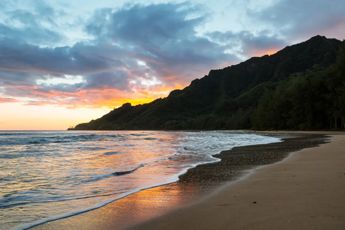Dramatic aerial view of Hāʻena State Park with Nāpali Coast cliffs, turquoise waters, and lush green mountains
