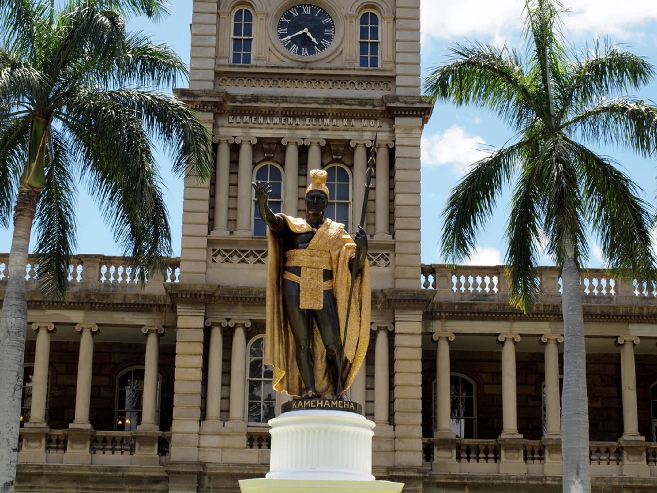 The painted Kamehameha statue in Kapaʻau with vibrant colors - rich brown skin, brilliant yellow feather cloak, and red sash - standing in front of the North Kohala Civic Center