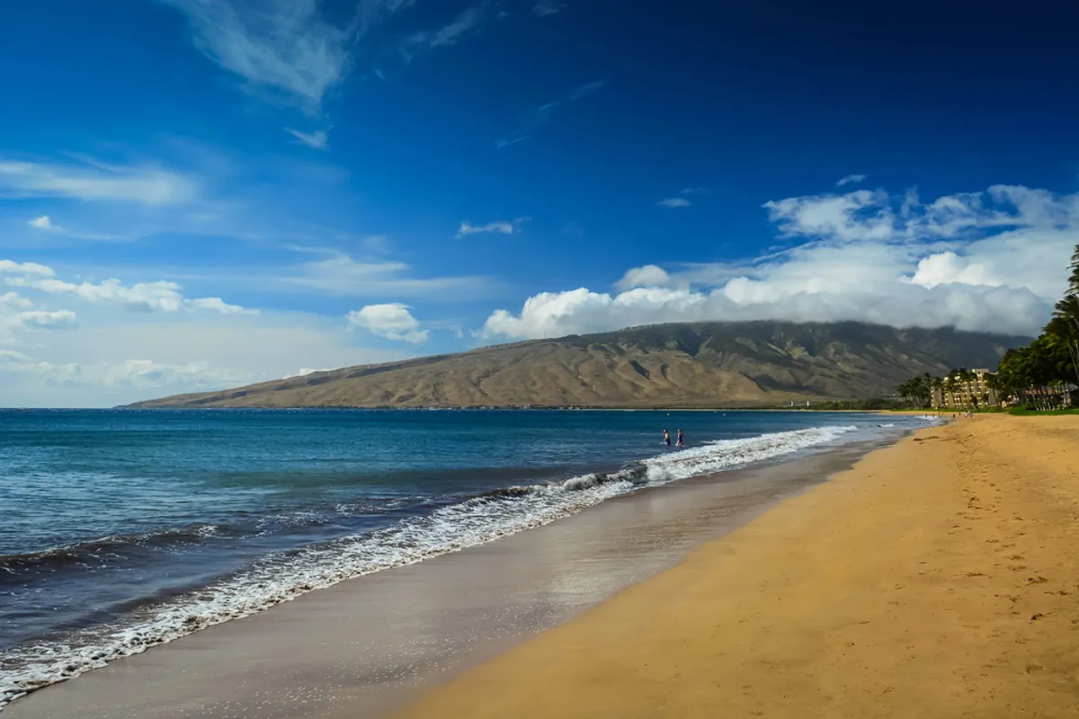 Kihei beach at sunset with golden light, rocky shoreline, and calm turquoise waters