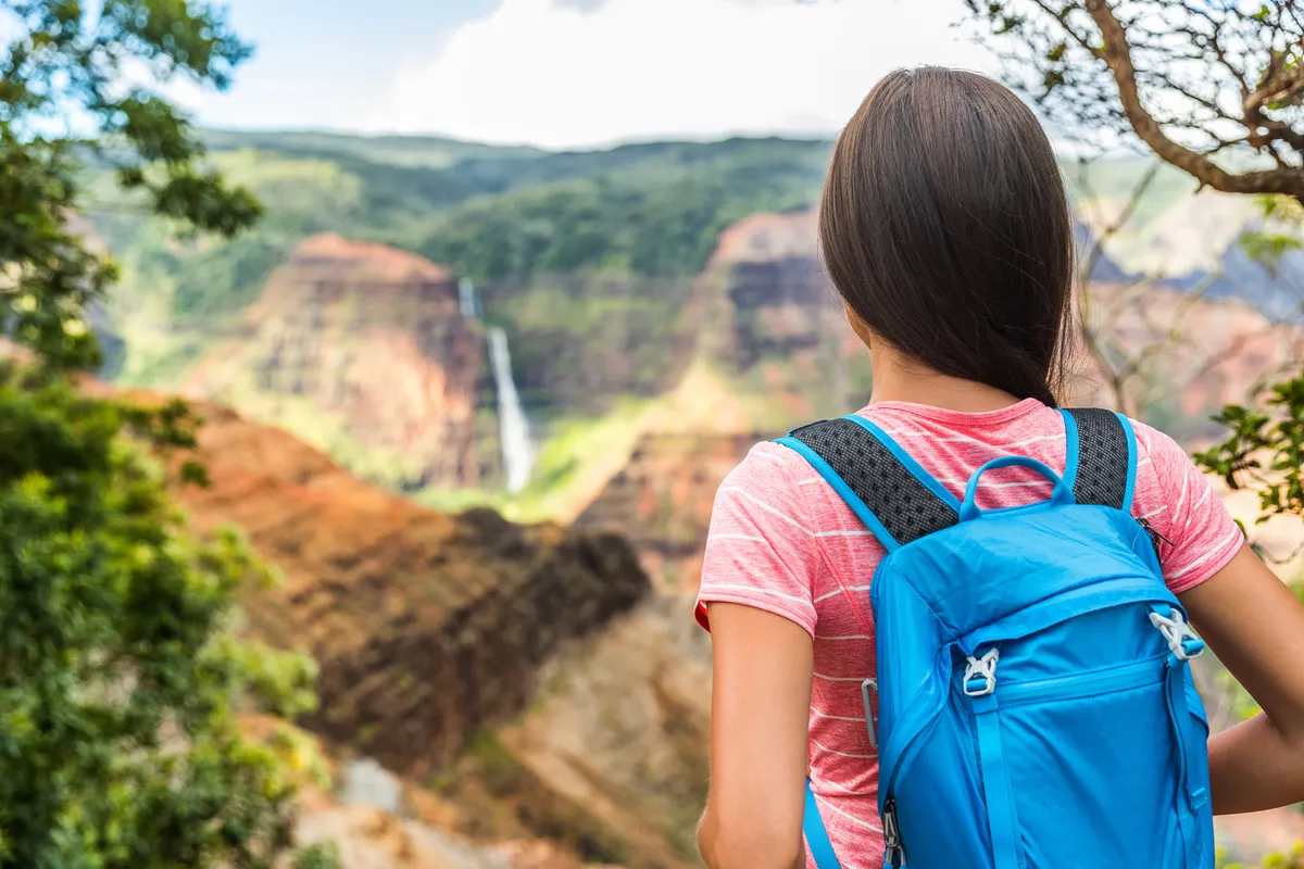 Woman celebrating at spectacular Big Island waterfall with arms raised in joy