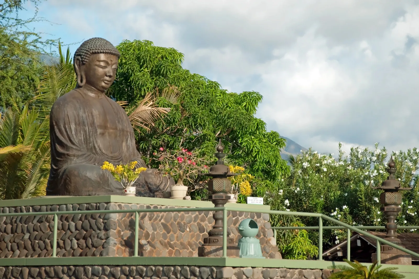 Great Amida Buddha statue at Lahaina Jodo Mission with West Maui mountains and tropical flowers