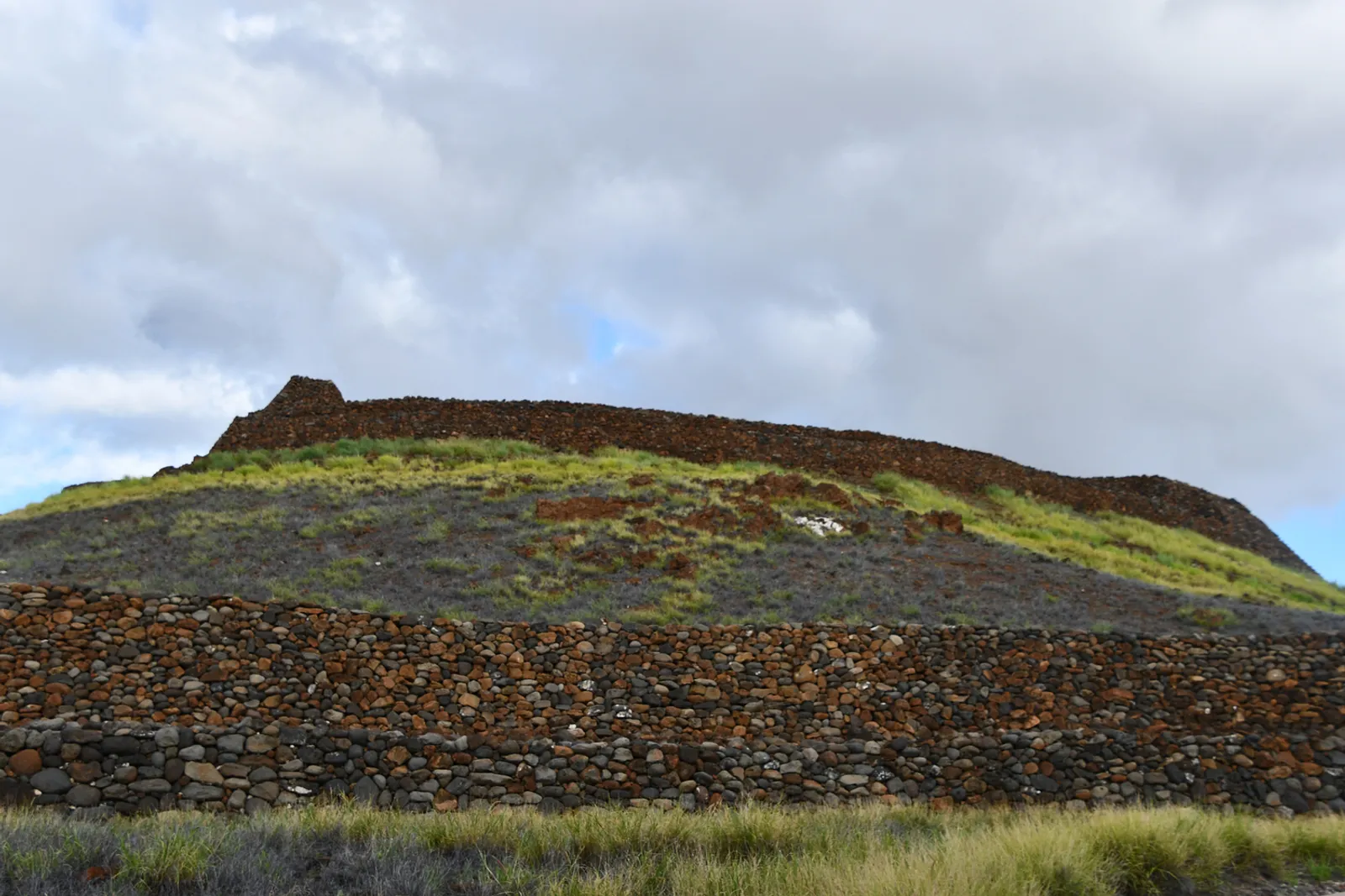 Ancient Hawaiian heiau (temple) with stone walls against dramatic volcanic landscape and ocean backdrop