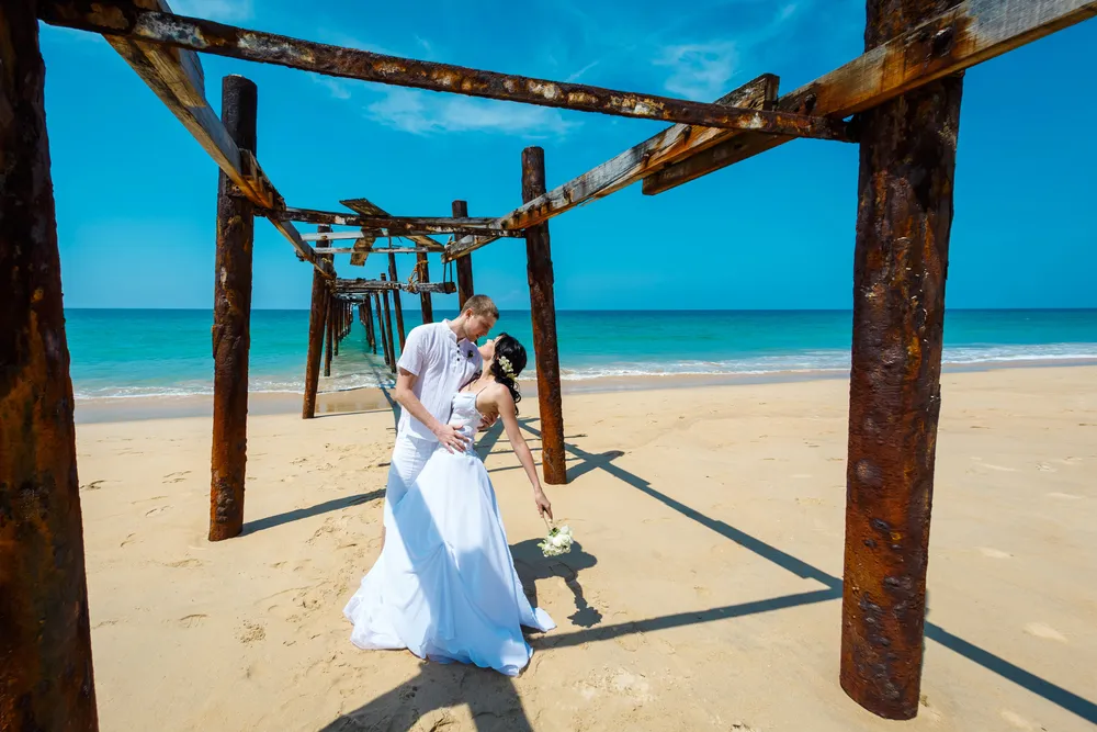 Romantic couple holding hands on a pristine Kauai beach with turquoise ocean and palm trees