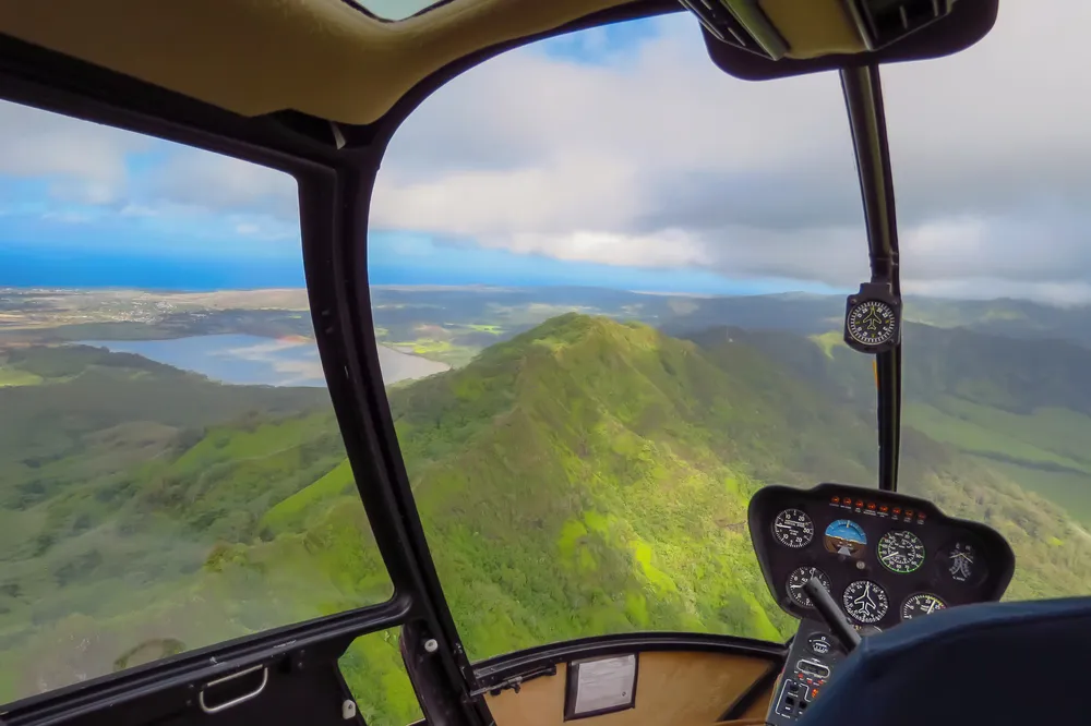 Inside a helicopter cockpit flying over Oahu's green mountains