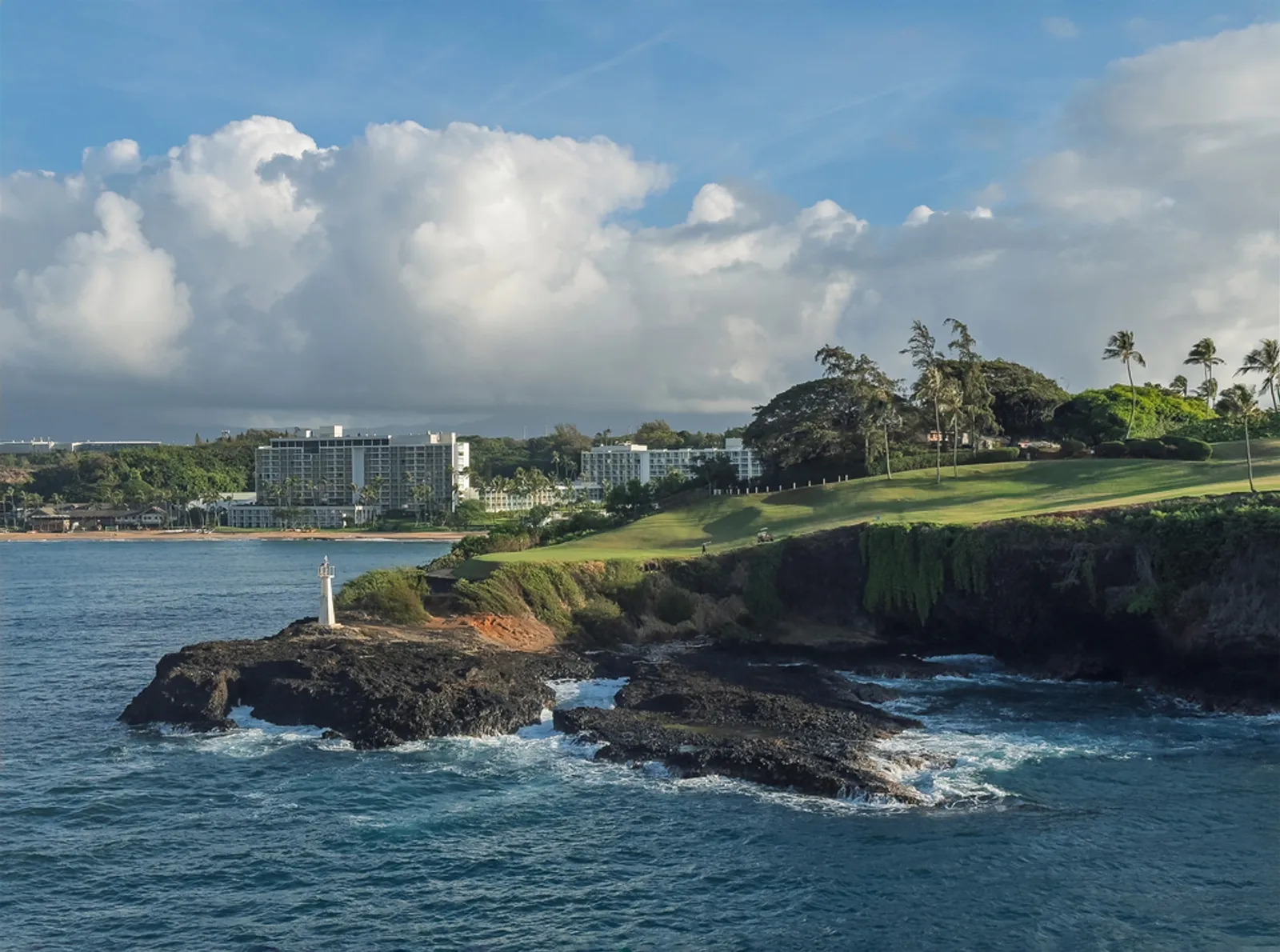 Oceanfront golf hole on Kauai with lush mountains in background