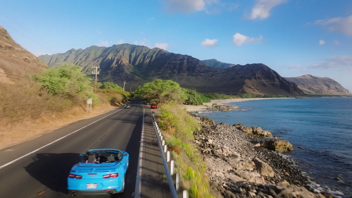 Aerial view of scenic Hawaiian road trip with car driving along tropical coastline