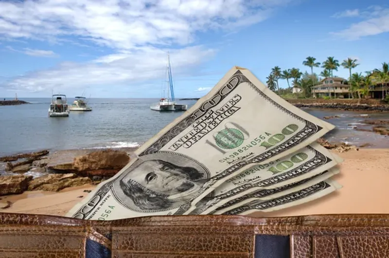 US dollar bills scattered on a wooden surface with a Hawaiian beach in the background