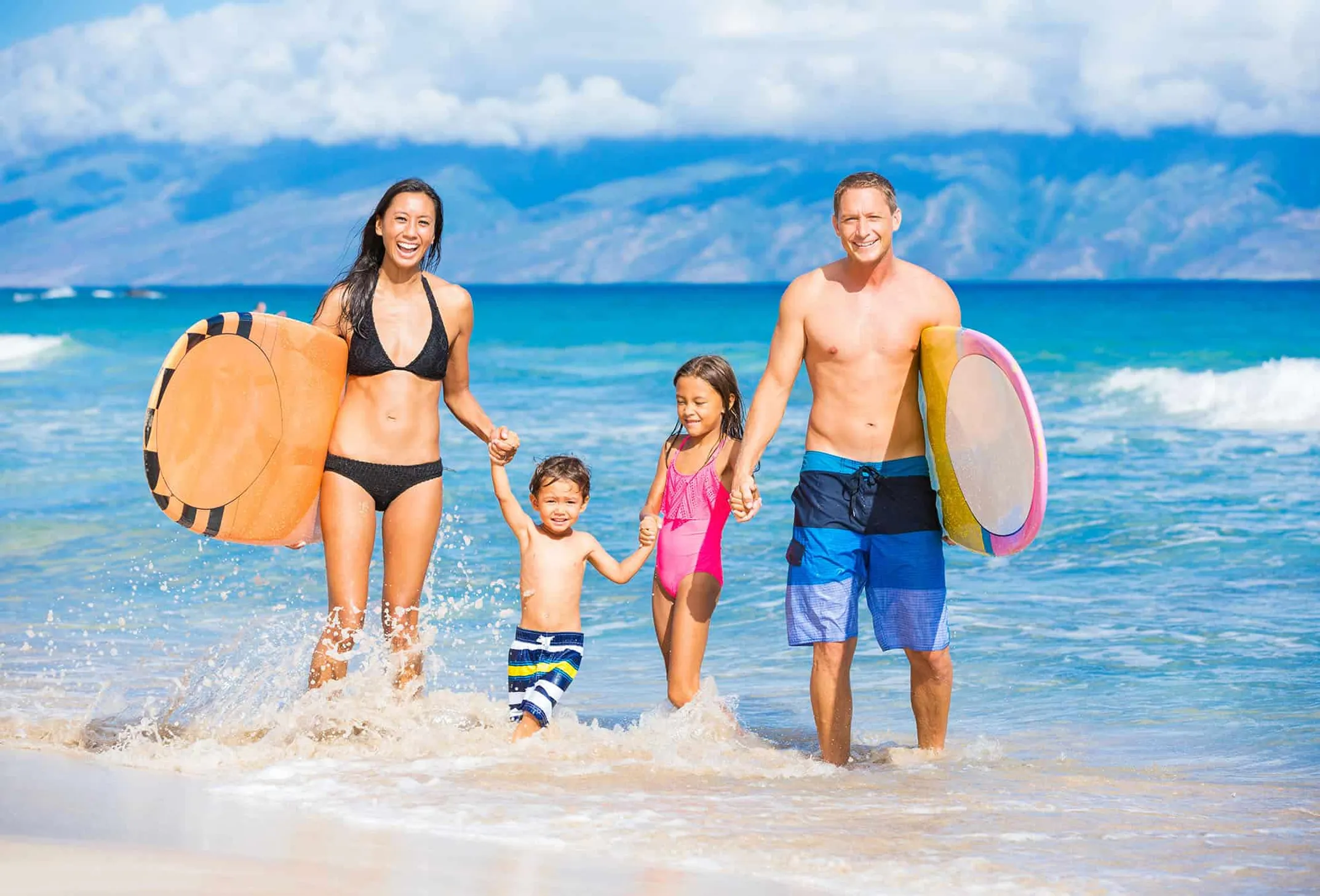 Hawaiian family enjoying beach activities with tropical mountains in background