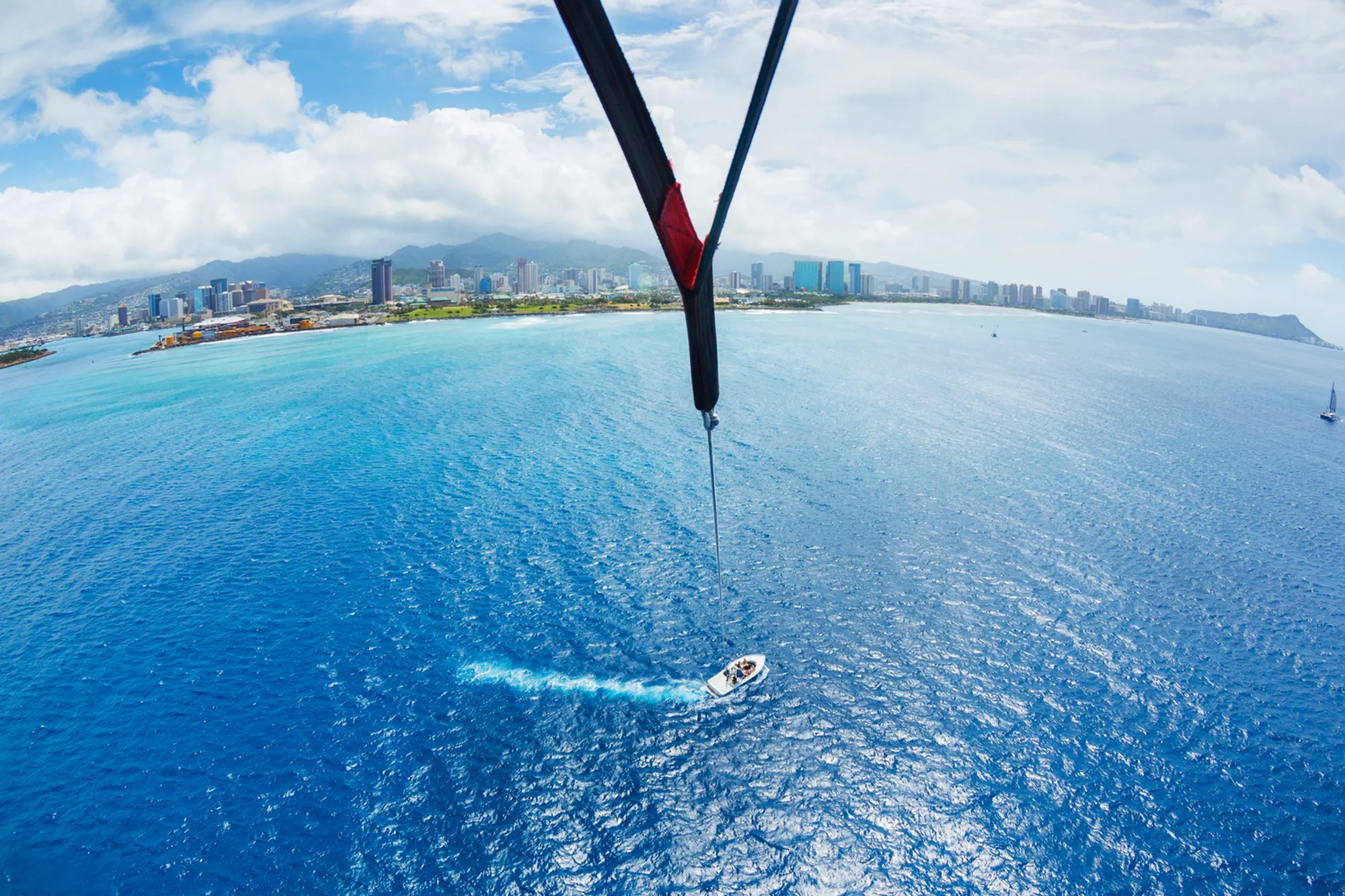 Person parasailing high above the crystal-clear blue waters of Hawaii with the coastline below