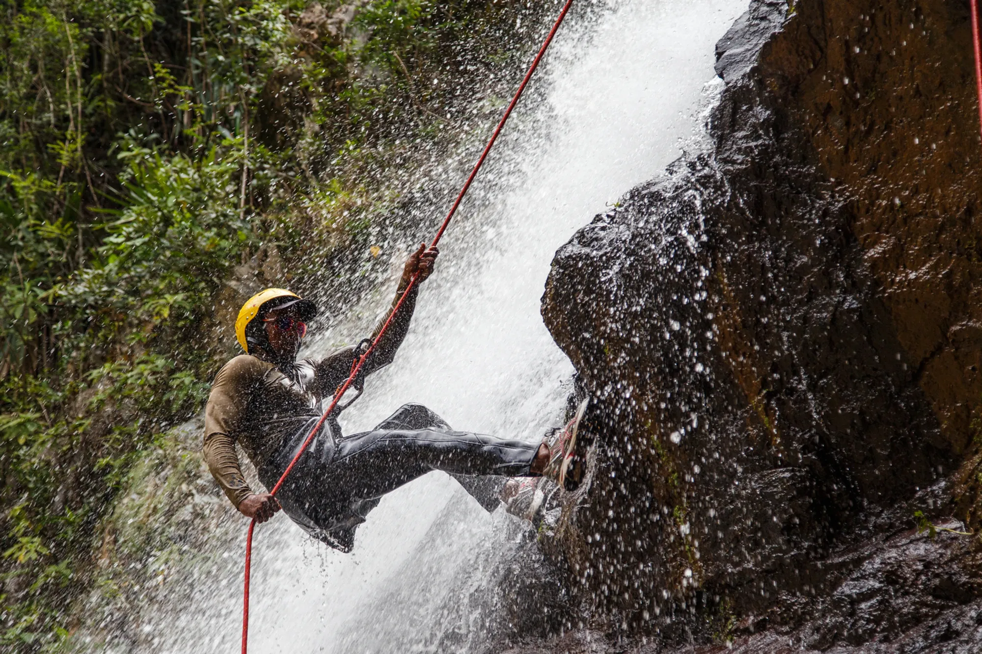 Adventurer rappelling down a dramatic Hawaiian waterfall surrounded by lush tropical rainforest