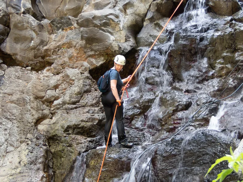Close-up of rappelling gear with waterfall and tropical vegetation in soft focus background