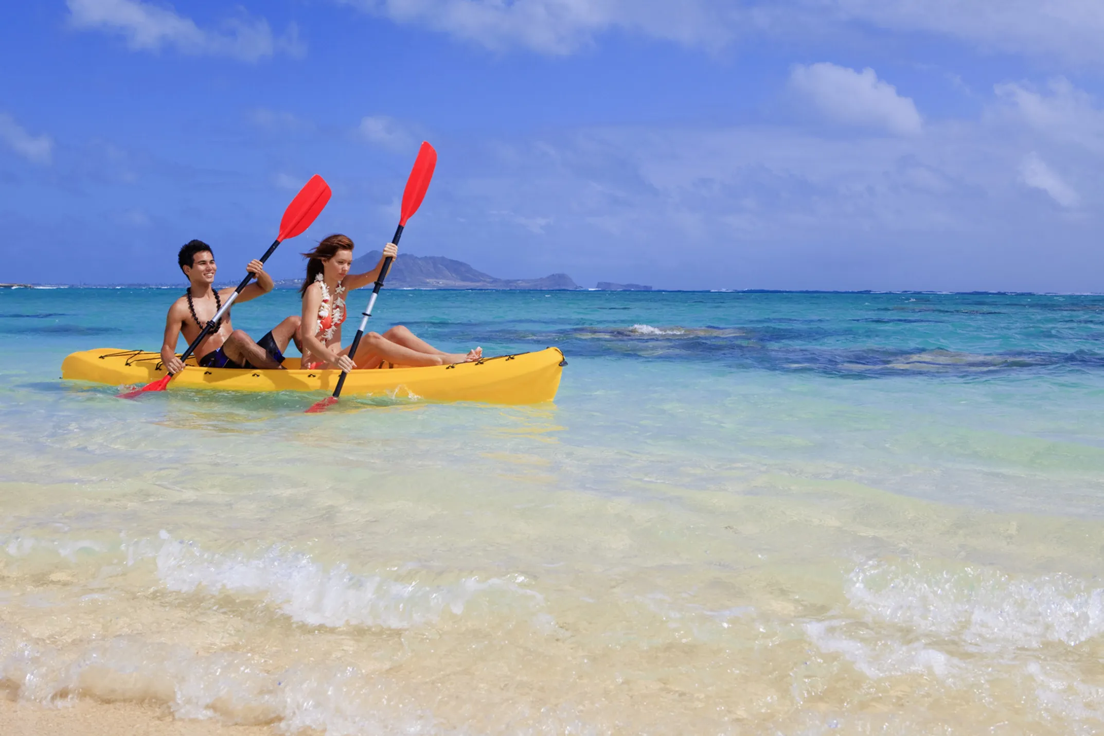 Romantic couple running together on a pristine Hawaiian beach with crystal clear water and mountains in the background