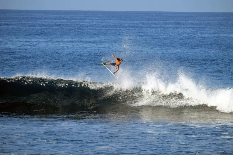 Ancient Hawaiian surfer on traditional koa board with modern surfers in background - symbolizing the continuity of surf culture