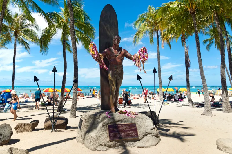 Duke Kahanamoku statue on Waikiki Beach with lei and visitors