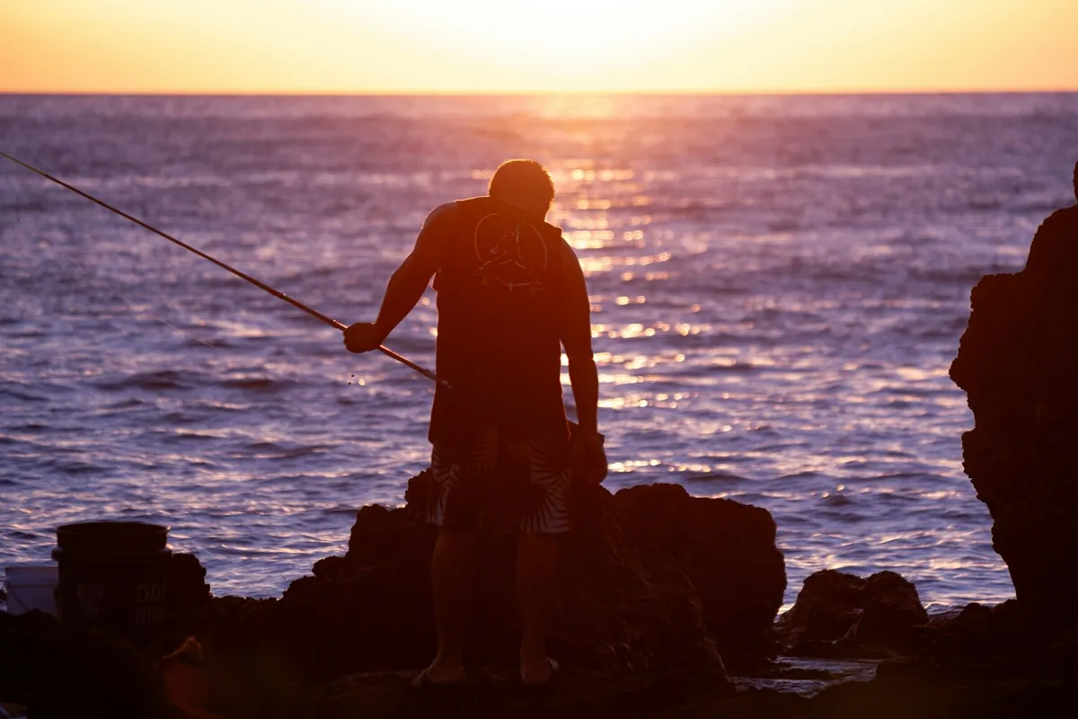 Angler with fishing rod at sunset showcasing responsible fishing practices in Hawaii