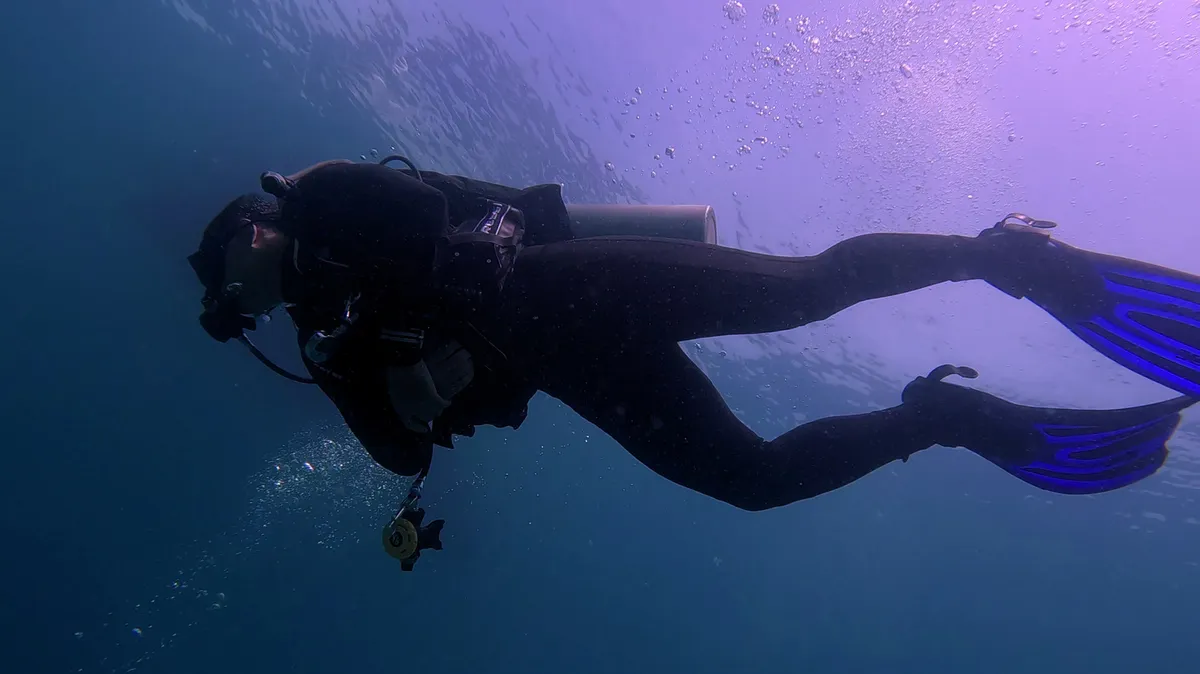 Scuba diver exploring open ocean with clear blue sky visible above water surface