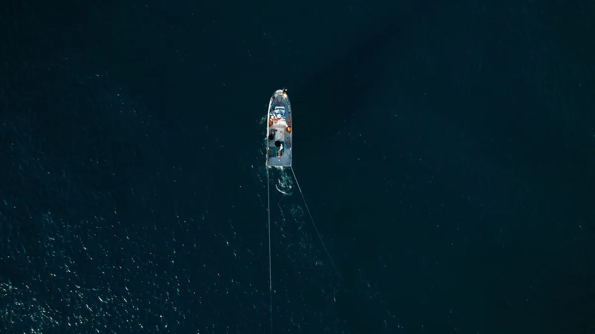 Aerial view of a small trawler boat moving through deep blue Hawaiian waters with fishermen ready for action